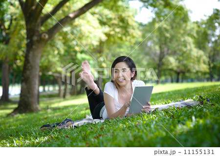 Young woman in a park wearing casual laying on a mat using mobile device tablet iPad 11155131