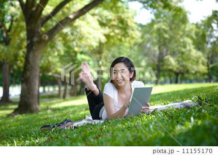 Young woman in a park wearing casual laying on a mat using mobile device tablet iPadYoung woman in a 11155170
