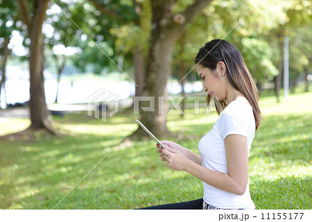 Young woman in a park wearing casual sitting on a mat using mobile device tablet iPad Young woman in a park wearing casual sitting on a mat using mobile device tablet iPad 11155177
