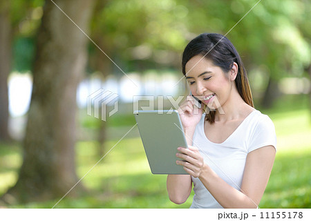 Young woman in a park wearing casual sitting on a mat using mobile device tablet iPad 11155178