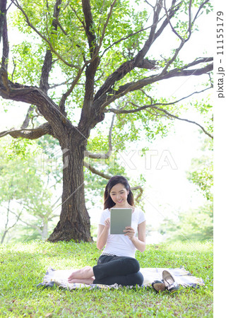 Young woman in a park wearing casual sitting on a mat using mobile device tablet iPad 11155179