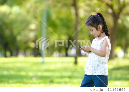 Little girl in casual using mobile smart phone in a park Little girl in casual using mobile smart phone in a park 11161642
