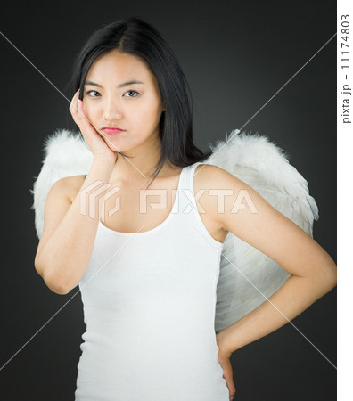 Upset Asian young woman dressed up as an angel with her hands on cheek and hand on hip 11174803