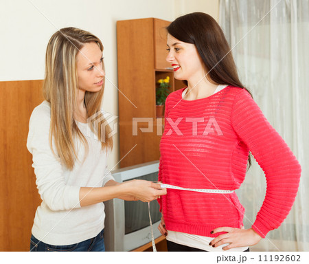 Young woman measuring waist of girlfriend 11192602