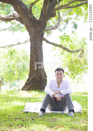 Young man in causal relaxing sitting on a mat in a park 11213480