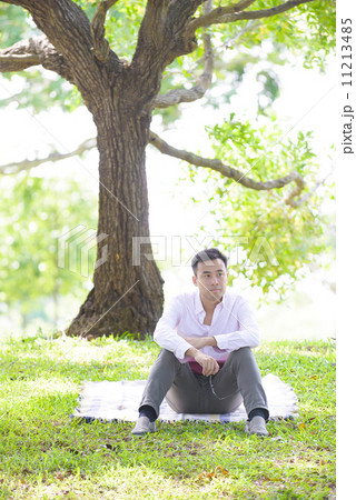 Young man in causal looking troubled sitting on a mat in a park Young man in causal looking troubled sitting on a mat in a park 11213485