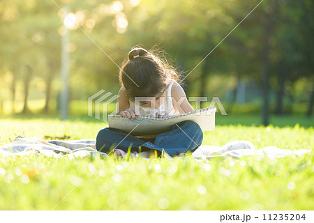 Little girl in casual sitting on a mat drawing in a park 11235204