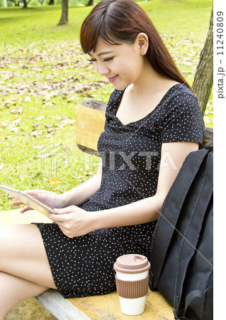 Beautiful student using tablet and drinking coffee in park Beautiful student using tablet and drinking coffee in park 11240809