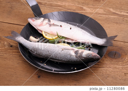 Two fresh sea bass fish on frying pan with lemon Two fresh sea bass fish on frying pan with lemon 11280086