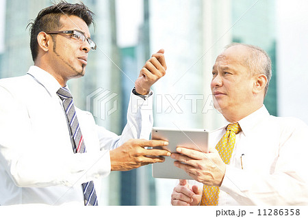 Young executive presenting to senior executive using tablet & pointing to a direction 11286358