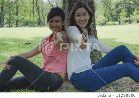 Two Girls Sitting Under a Tree in a park 11298586