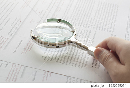 Hand holding magnifying glass to read document 11306364
