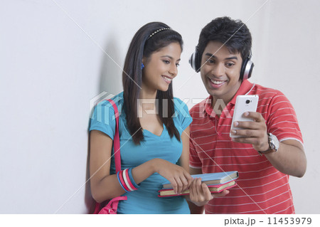 Happy university friends reading text message on smart phone against wall Happy university friends reading text message on smart phone against wall 11453979