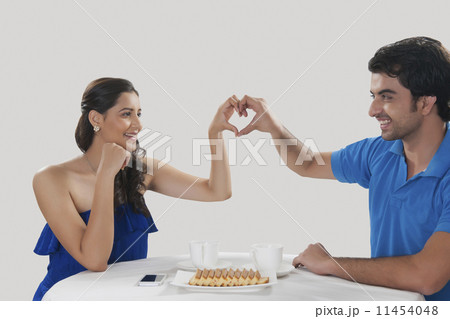 Happy young couple making heart shape sign while having coffee against white background 11454048
