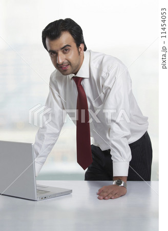 Portrait of young businessman with laptop at office desk 11454053