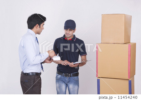 Businessman conversing with delivery man by stacked packages against gray background 11454240