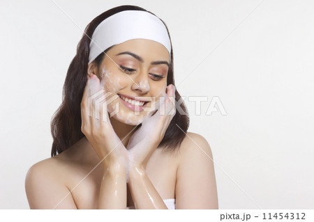 Smiling woman applying soap on face against white background 11454312
