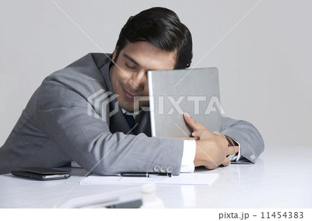 Loving businessman embracing laptop at desk over gray background 11454383