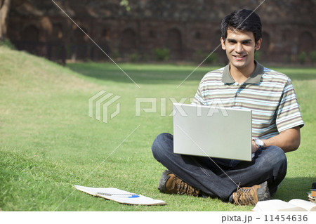 Student with a laptop sitting in a park 11454636