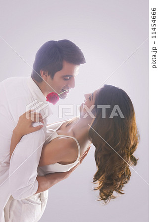 Romantic young man holding red rose in mouth while dancing with woman over white background Romantic young man holding red rose in mouth while dancing with woman over white background 11454666