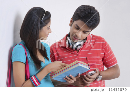 Young university students discussing over book against wall 11455079