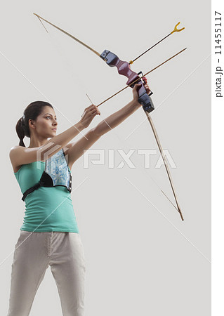 Young female archer practicing archery against gray background 11455117