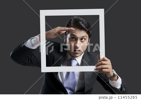 Young businessman shielding eyes while holding frame over black background Young businessman shielding eyes while holding frame over black background 11455265