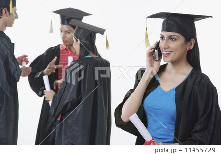 Smiling graduate student answering mobile phone with friends discussing against white background 11455729