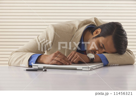 Young businessman sleeping on laptop at desk in office Young businessman sleeping on laptop at desk in office 11456321
