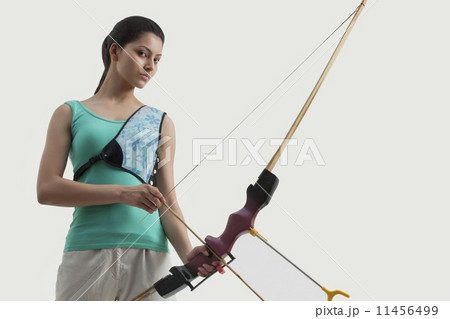 Portrait of female archer with bow and arrow isolated over gray background 11456499
