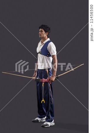Full length of young male archer with bow and arrow over gray background Full length of young male archer with bow and arrow over gray background 11456500