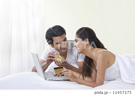 Happy couple buying ring online with credit card in bed 11457275