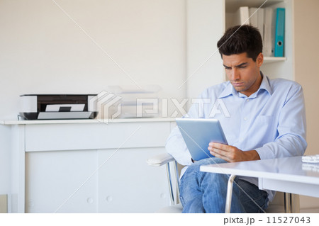Casual businessman using his tablet at his desk Casual businessman using his tablet at his desk 11527043