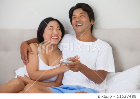 Happy couple lying on bed together watching tv Happy couple lying on bed together watching tv 11527489