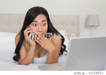 Shocked woman looking at laptop on the phone 11528351