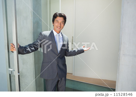 Confident estate agent standing at front door welcoming you in 11528546