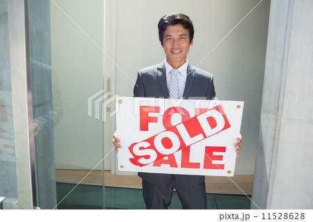 Confident estate agent standing at front door showing sold sign 11528628