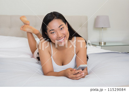 Happy woman lying on bed holding smartphone Happy woman lying on bed holding smartphone 11529084