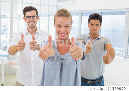 Casual business team smiling at camera with thumbs up 11529090