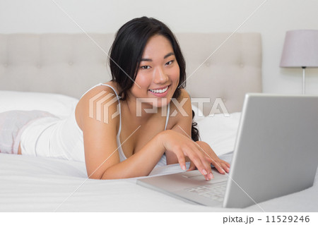 Happy woman lying on bed using laptop Happy woman lying on bed using laptop 11529246