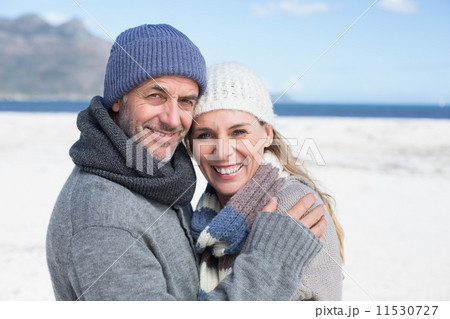 Attractive couple smiling at camera on the beach in warm clothin 11530727