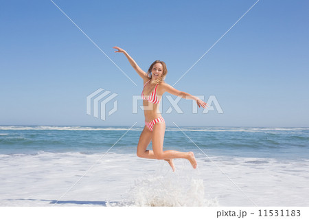 Happy fit woman in bikini jumping on the beach 11531183