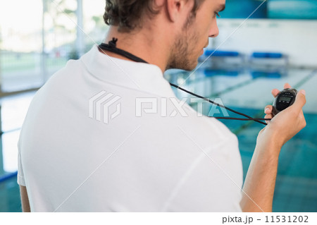 Swimming coach standing by the pool looking at stopwatch 11531202
