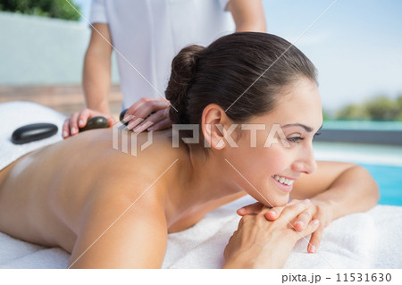 Happy brunette getting a hot stone massage poolside Happy brunette getting a hot stone massage poolside 11531630