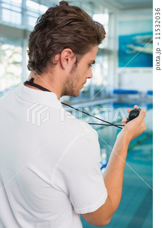 Swimming coach standing by the pool looking at stopwatch Swimming coach standing by the pool looking at stopwatch 11532036