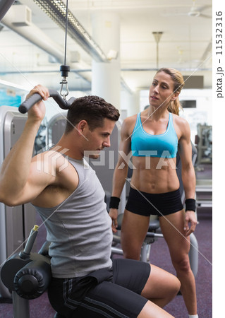 Bodybuilder using weight machine for arms with encouraging train 11532316