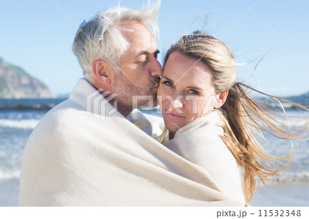 Smiling couple wrapped up in blanket on the beach Smiling couple wrapped up in blanket on the beach 11532348