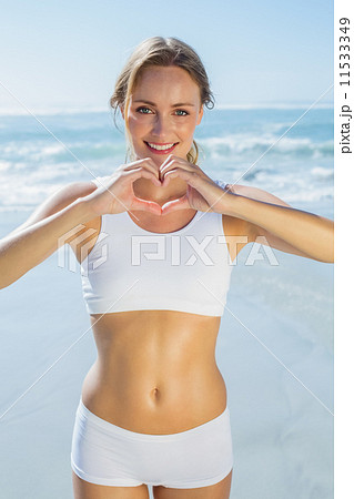 Gorgeous fit blonde making heart shape with hands by the sea 11533349