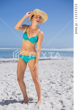 Pretty laughing woman in bikini on beach wearing sunhat 11533523