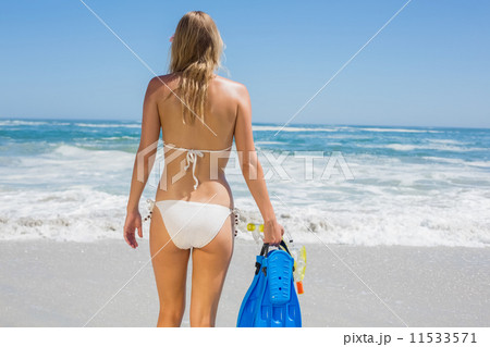 Fit woman in white bikini holding snorkeling gear on the beach 11533571